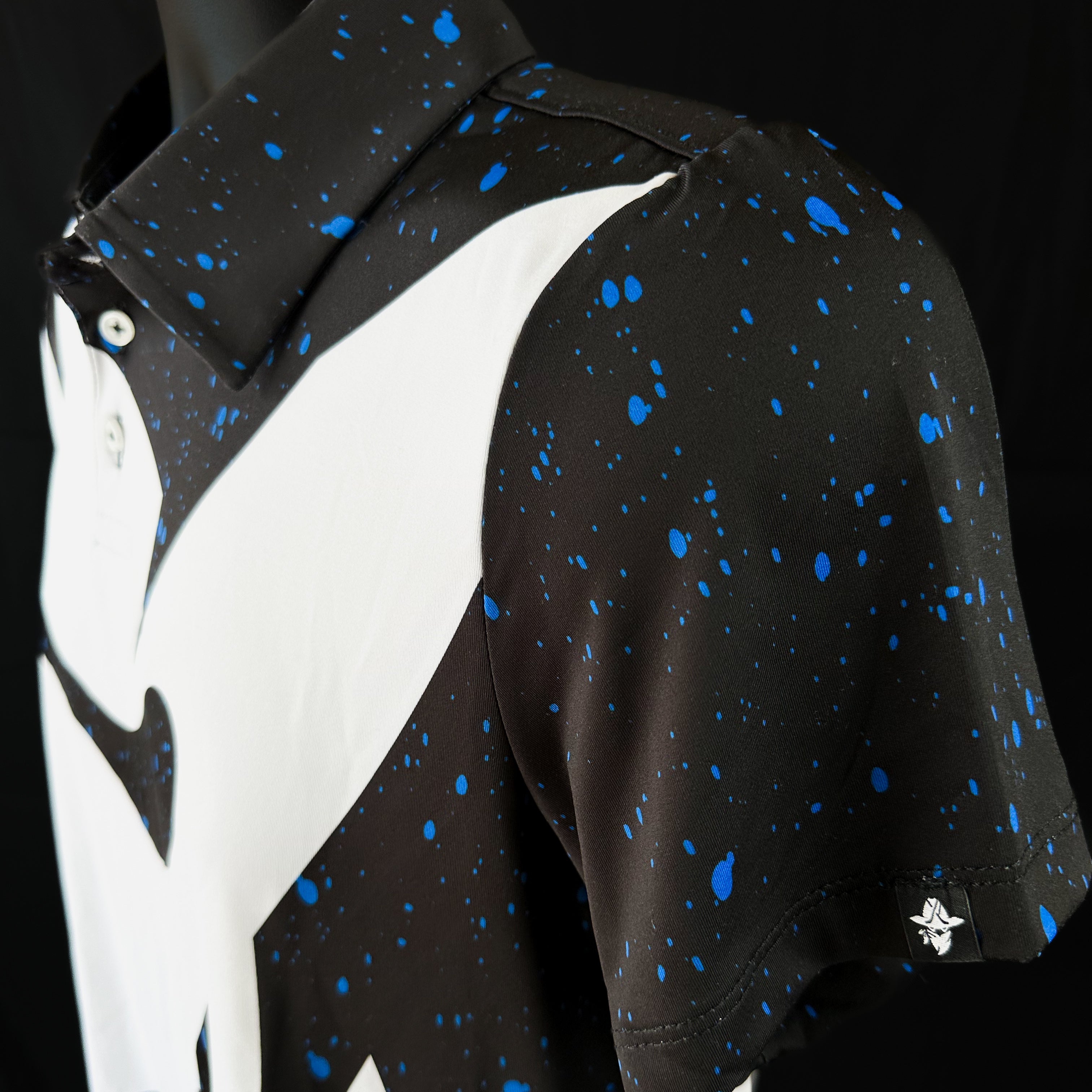 Close-up side view of Bandito Blitz Boys Junior Golf Polo in bold black and white graphic design with blue speckles, showcasing moisture-wicking fabric, SPF 50 protection, wrinkle-resistance, and 4-way stretch. Perfect junior golf clothing for boys aged 8-14. Golf Bandit Junior Golf Polos are the best quality in US Kids Golf apparel.