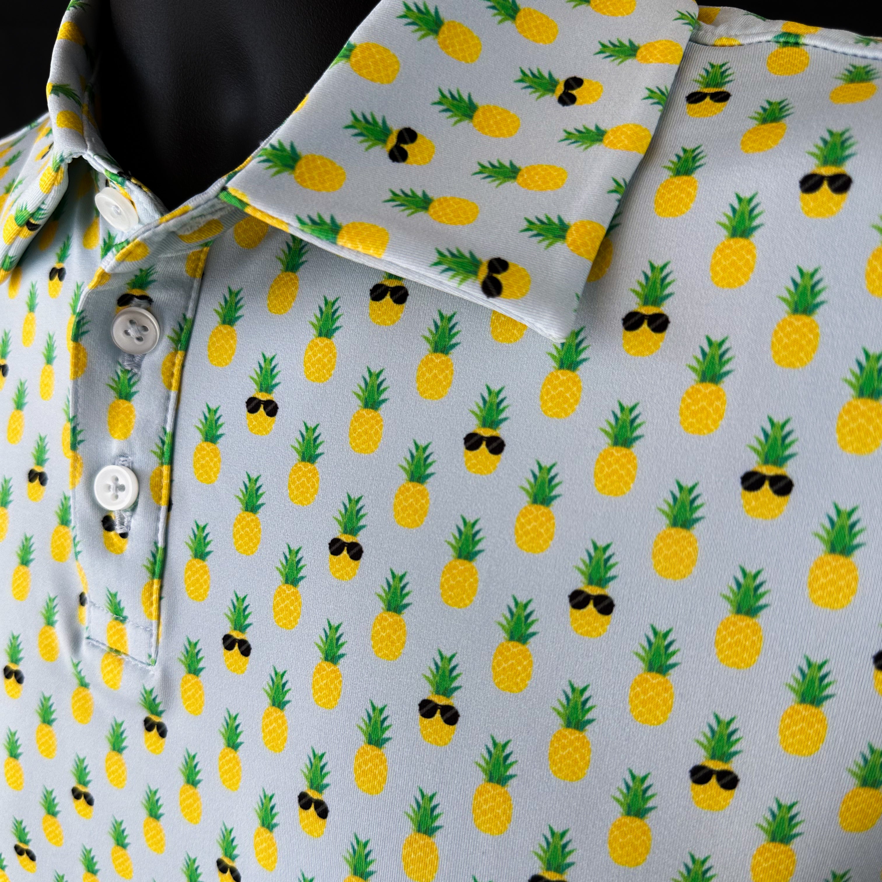 Close-up collar of La Piña Girls Junior Golf Polo in light blue with playful pineapple print, showcasing moisture-wicking fabric, SPF 50 protection, wrinkle-resistance, and 4-way stretch. Perfect junior golf clothing for girls aged 8-14. Golf Bandit Junior Golf Polos are the best quality in US Kids Golf apparel.