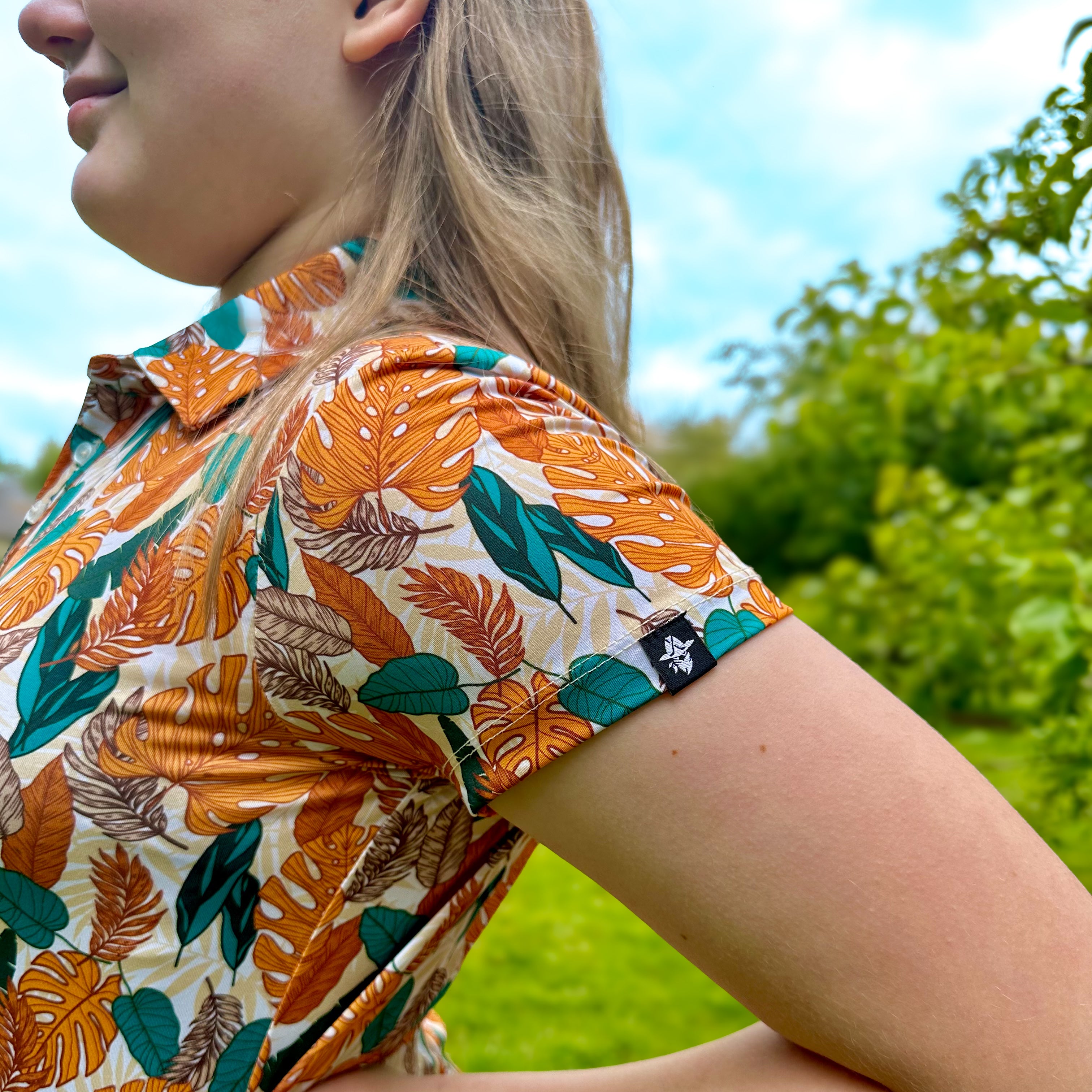 Girl wearing Paradise Greens Girls Junior Golf Polo in a vibrant leafy design, showcasing moisture-wicking fabric, SPF 50 protection, wrinkle-resistance, and 4-way stretch. Perfect junior golf clothing for girls aged 8-14. Golf Bandit Junior Golf Polos are the best quality in US Kids Golf apparel.